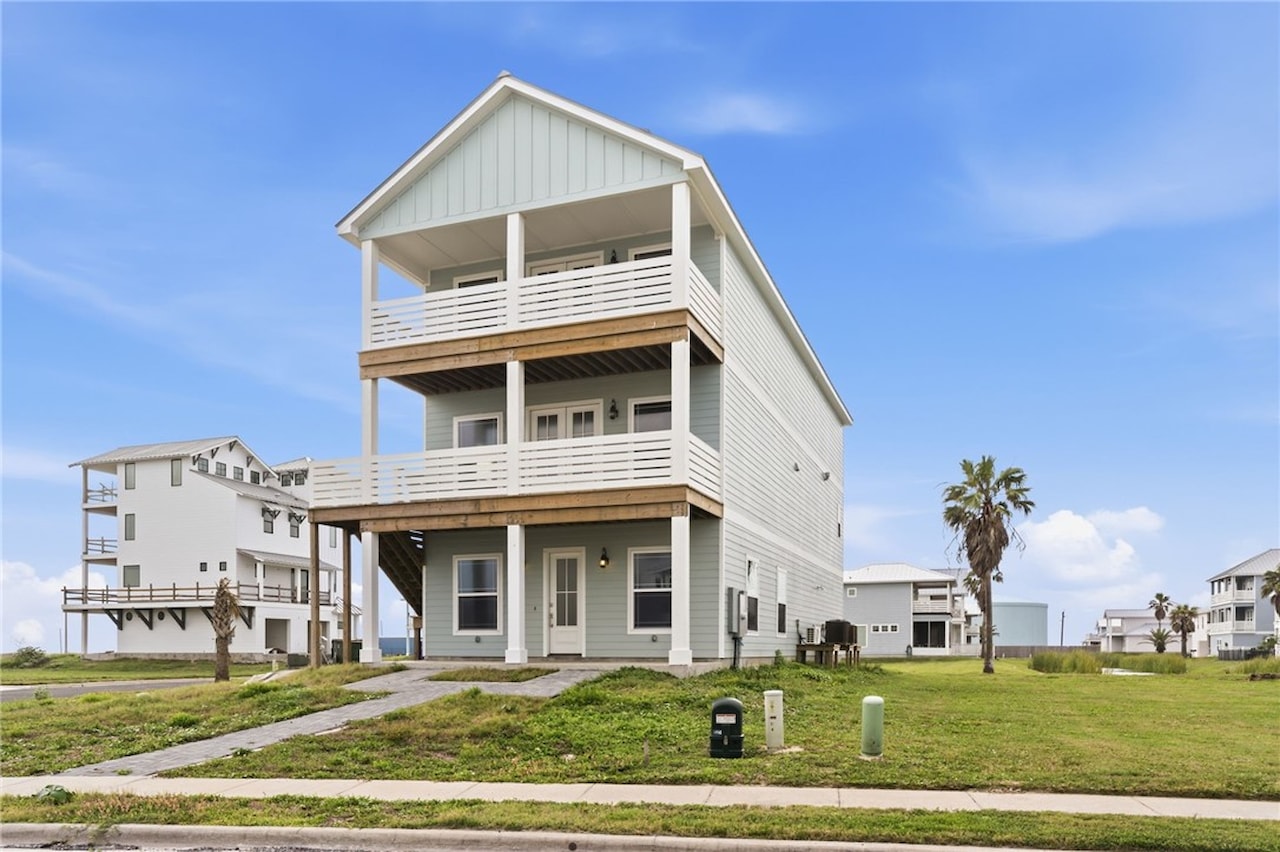 Daytime front elevation of 8118 Beach Break Drive showing the sage-green three-story coastal facade with double-stacked covered balconies and a palm tree
