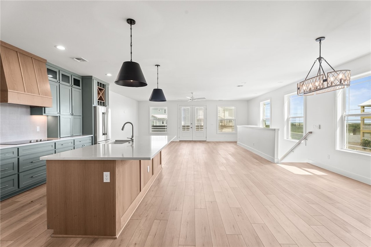 Open second-floor living level looking through the kitchen toward the great room, with French doors to a balcony, a beaded chandelier and light oak floors