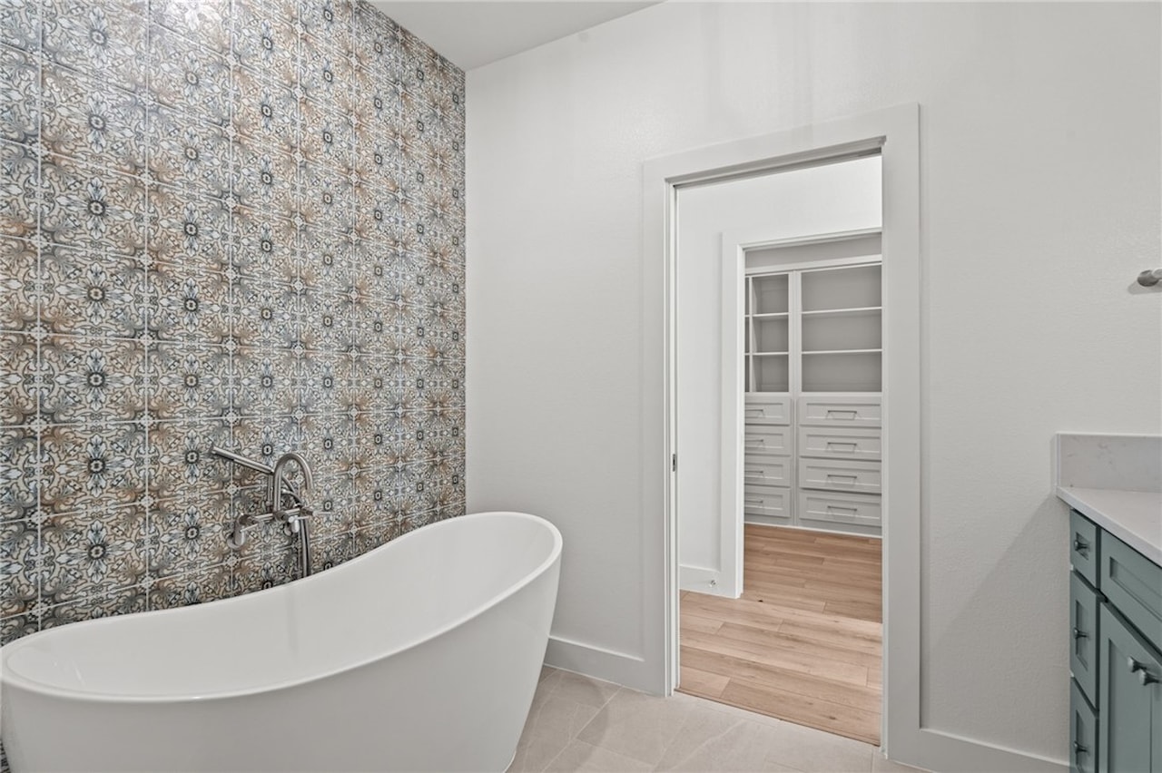 Primary bath with a freestanding soaking tub against a patterned blue and rust decorative tile feature wall, opening into a walk-in closet