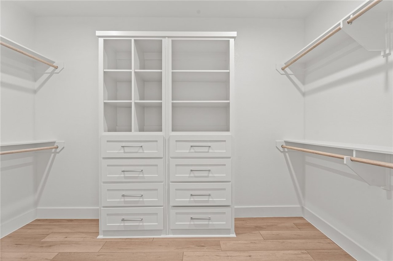 Walk-in closet with built-in white drawers and open shelving along the wall over light oak flooring