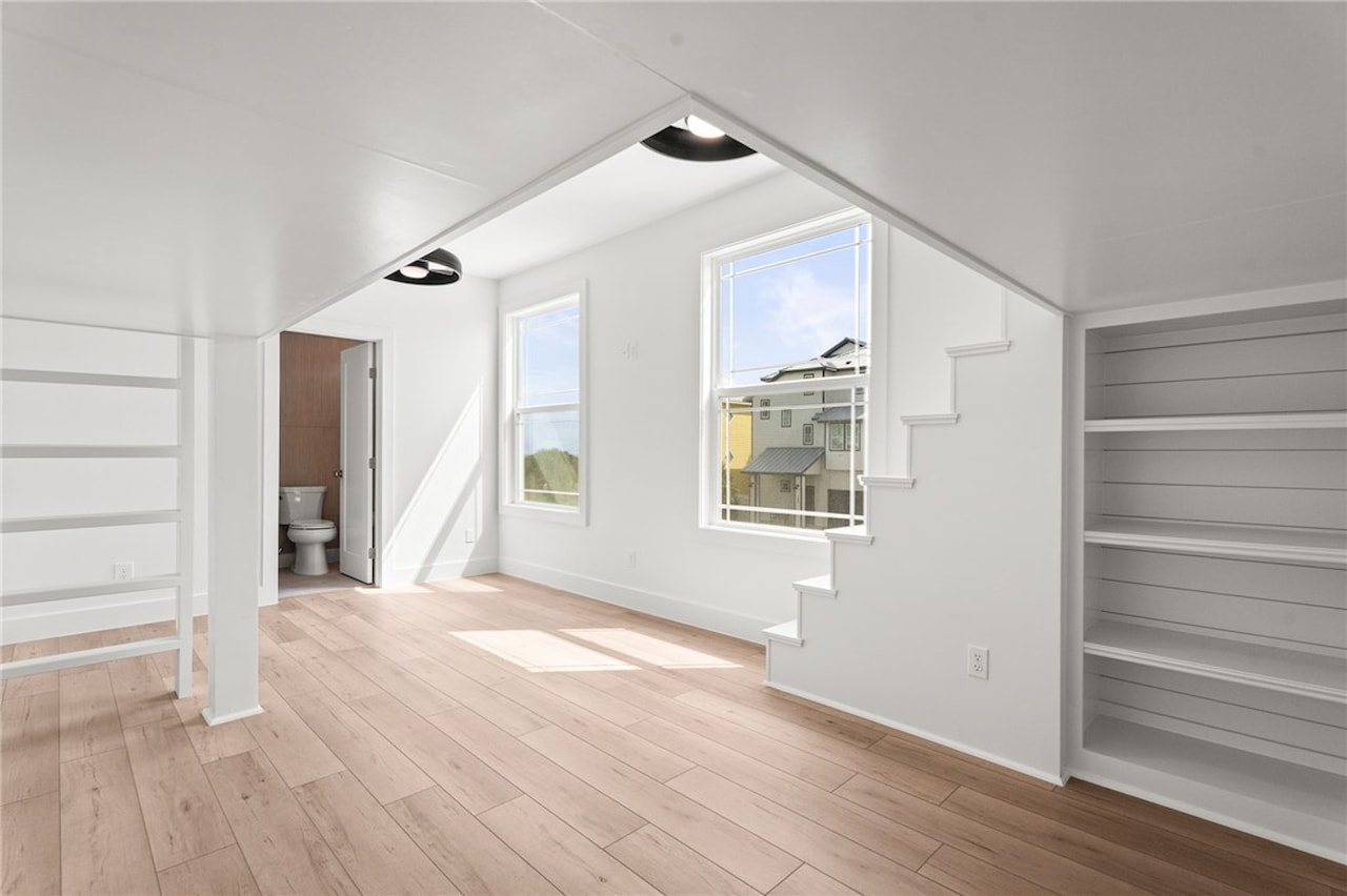 Third-floor flex room with a sloped vaulted ceiling, built-in shelving niches, two windows looking onto neighboring homes and an attached full bath