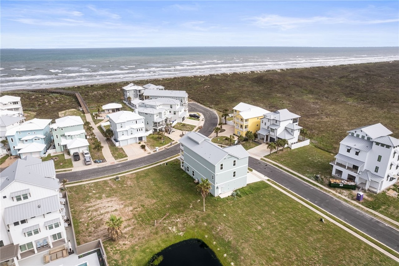 Aerial of 8118 Beach Break Drive on its lot in Island Park Estates with neighboring coastal homes and the Gulf of Mexico shoreline directly behind