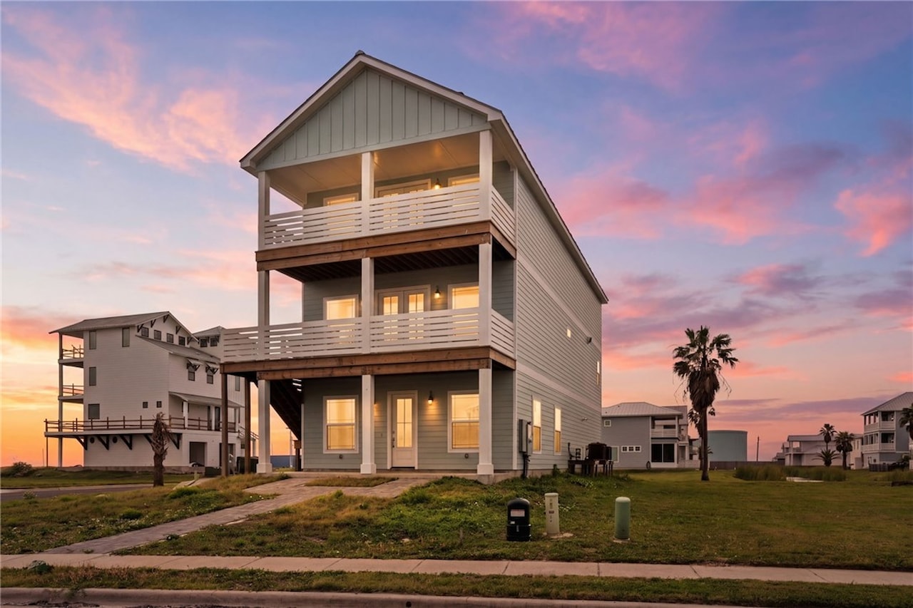 Twilight view of 8118 Beach Break Drive, a three-story elevated coastal home with stacked balconies lit against a pink dusk sky on Mustang Island